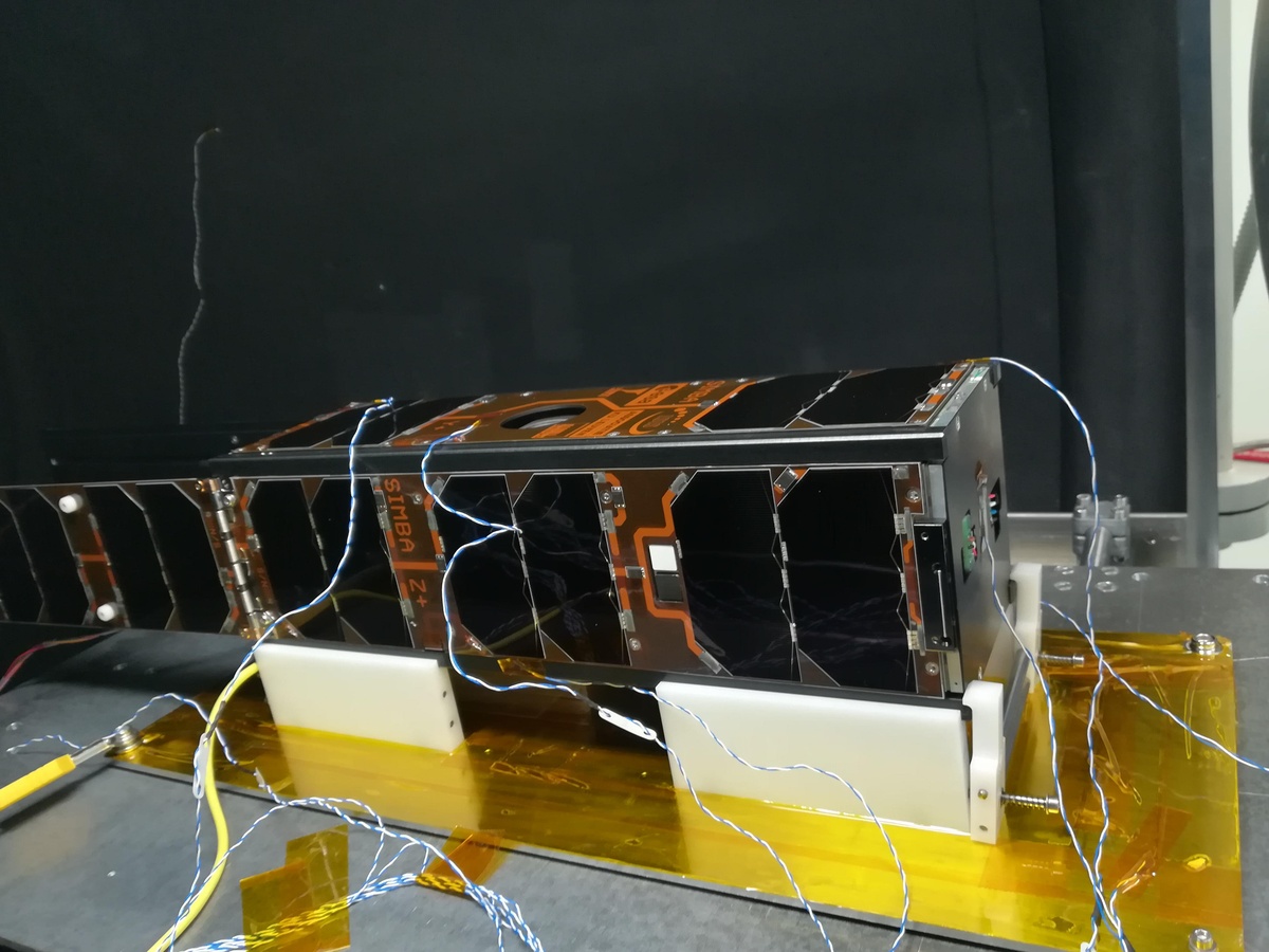 SIMBA klaar om in de thermische vacuümkamer te gaan. We zien nu de achterkant van de satelliet met de zonnepanelen en twee spectrale sensoren. De draadjes zijn verbonden met thermokoppels om de temperatuur van de satelliet in de gaten te houden tijdens de test.